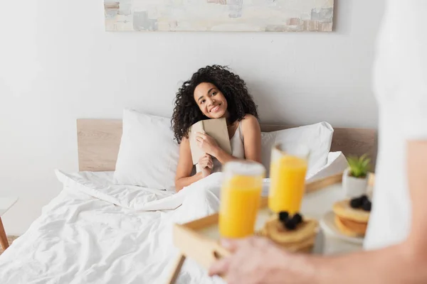 Blurred Man Holding Tray Breakfast Happy African American Girlfriend Book — Stock Photo, Image