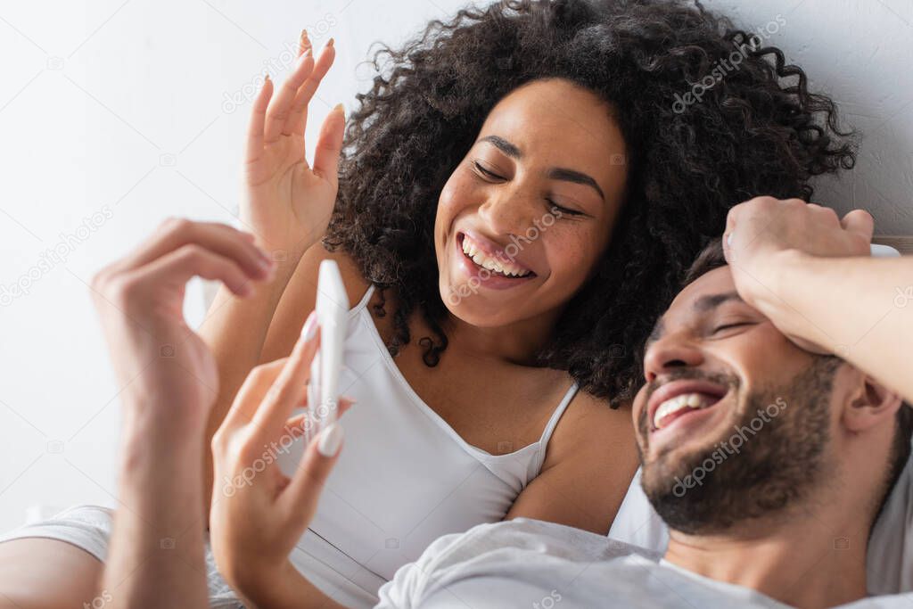 cheerful multiethnic couple smiling while looking at mobile phone 