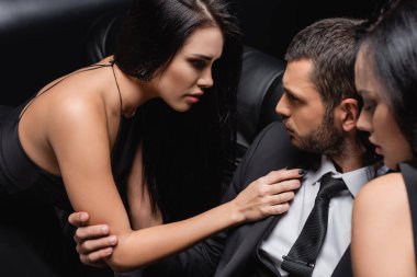 Genç ve başarılı iş adamının yanındaki baştan çıkarıcı kadınlar siyah arka planda.