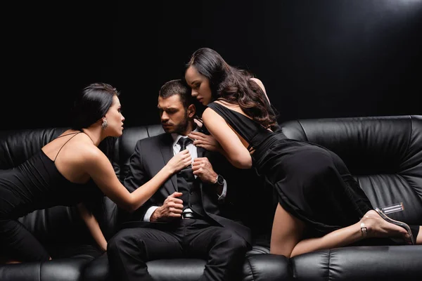 黒の革のソファに座っているビジネスマンを誘惑するセクシーでエレガントな女性 — ストック写真