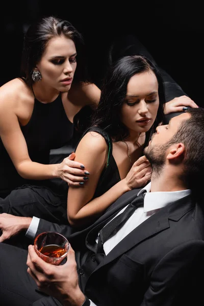 Hombre Sosteniendo Vaso Whisky Cerca Mujeres Sexy Seduciéndolo Aislado Negro — Foto de Stock