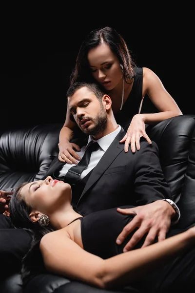 Hombre Traje Sentado Sofá Cuero Cerca Mujeres Seductoras Aisladas Negro — Foto de Stock