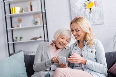 Oturma odasındaki kanepede akıllı telefon kullanan neşeli kadınlar. 