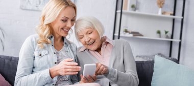Yaşlı anne ve pankartın yanındaki akıllı telefonu işaret eden kadın. 