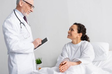 Mutlu Afro-Amerikan kadının yanında dijital tablet tutan gülümseyen doktor hastanede.