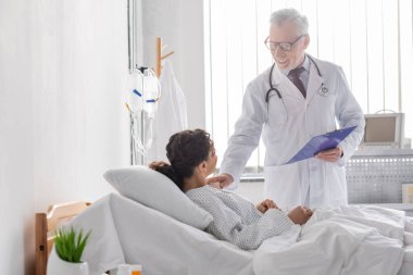 Afro-Amerikan bir kadının omzuna dokunurken elinde dosya tutan neşeli bir doktor.