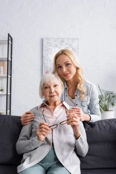 Mujer Abrazando Anciana Madre Con Anteojos Sofá — Foto de Stock