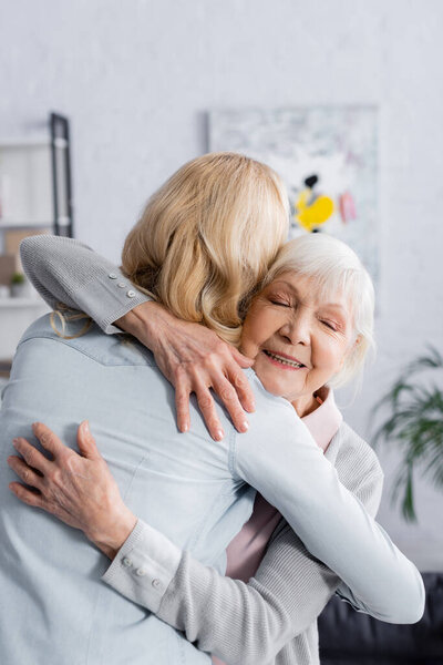 Smiling senior woman with closed eyes embracing adult daughter 