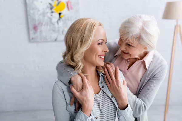 Leende Kvinna Som Rör Vid Gråhåriga Mammas Händer Hemma — Stockfoto