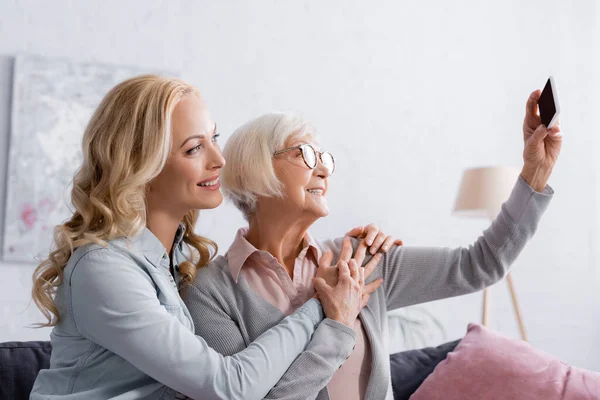 Mujer Sonriente Abrazando Madre Tomando Selfie Casa — Foto de Stock