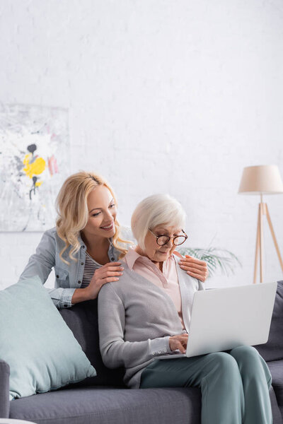 Smiling woman hugging senior parent using laptop 