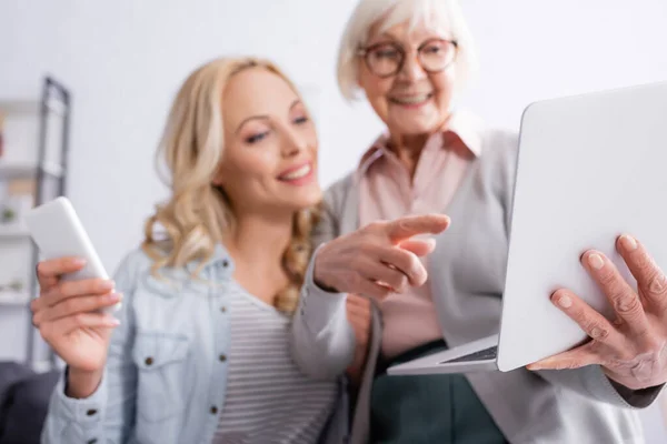 Senior Woman Blurred Background Pointing Laptop Daughter Smartphone — Stock Photo, Image