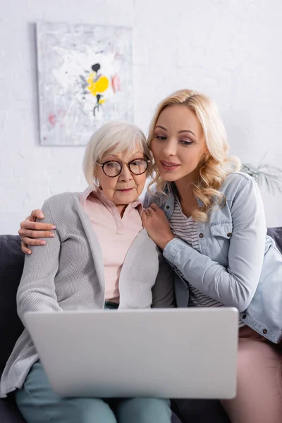 Mulher Abraçando Mãe Sênior Perto Laptop Borrado Sofá — Fotografia de Stock