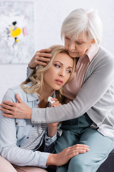 Пожилая женщина обнимает недовольную дочь в гостиной 