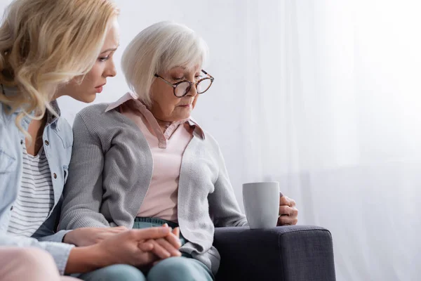 Ontevreden Senior Vrouw Houdt Beker Buurt Trieste Dochter Wazig Voorgrond — Stockfoto