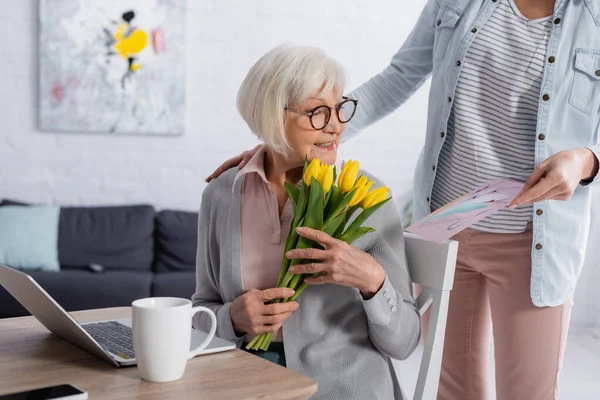 Fröhliche Ältere Frau Hält Tulpen Neben Tochter Mit Grußkarte Und — Stockfoto