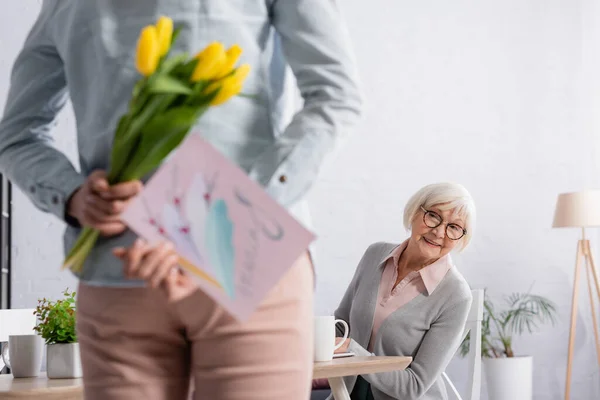 Sorridente Donna Anziana Seduta Vicino Figlia Che Tiene Fiori Biglietto — Foto Stock