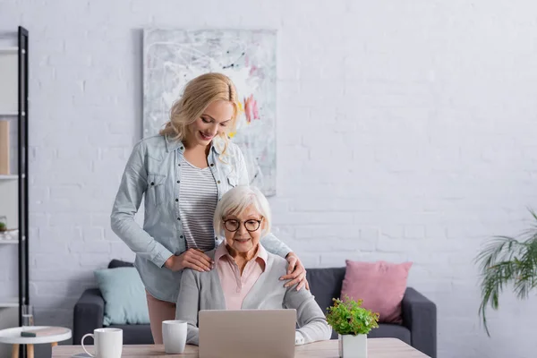 Glimlachende Vrouw Buurt Van Senior Moeder Met Behulp Van Laptop — Stockfoto