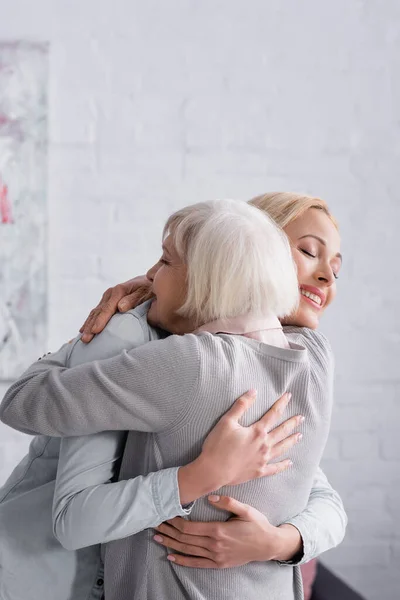 快乐的女人在客厅里拥抱灰白头发的父母 — 图库照片