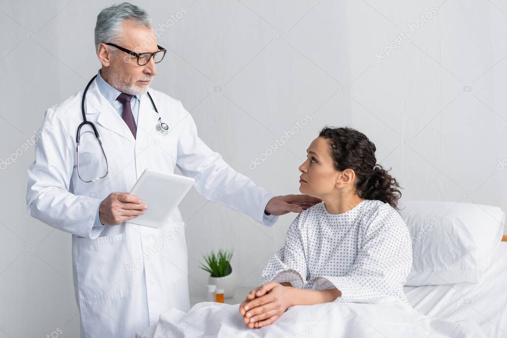 mature doctor touching shoulder of african american woman while holding digital tablet