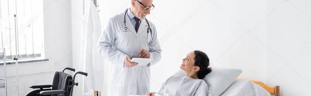 positive doctor talking to smiling african american woman in hospital, banner
