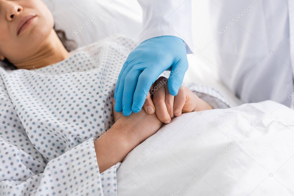 partial view of doctor in latex glove touching hands of diseased african american woman in hospital