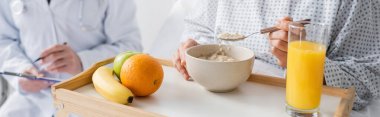 cropped view of woman eating oatmeal near fresh fruits and doctor on blurred background, banner clipart