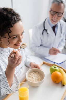 Gülümseyen Afrikalı Amerikalı kadın bulanık arka planda doktorun yanında mısır gevreği yiyor.