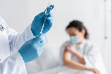 Tıbbi maskeli bulanık Afrikalı Amerikalı kadın lateks eldivenli, elinde şırınga ve aşı şişesi olan doktorun yanında.