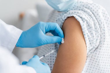 Lateks eldivenli doktorun tıbbi maskeli kadına aşı enjekte edişinin kısmi görüntüsü