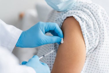 partial view of doctor in latex gloves doing injection of vaccine to woman in medical mask clipart