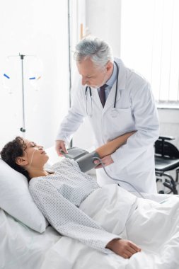 Orta yaşlı doktor, Afrikalı Amerikalı bir kadının klinikteki kan basıncını ölçecek.