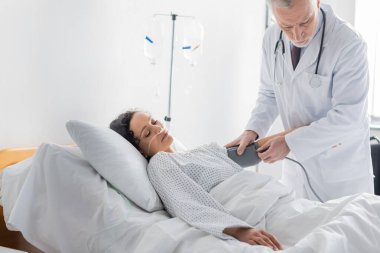 Hastane yatağında yatan Afrikalı Amerikalı bir kadının tansiyonunu ölçen doktor.