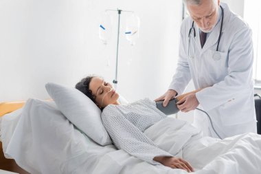 doctor measuring blood pressure of african american woman lying in hospital bed clipart