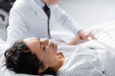 Burun kanülü hasta Afrikalı Amerikalı kadın bulanık arka planda doktorun yanında yatıyor.