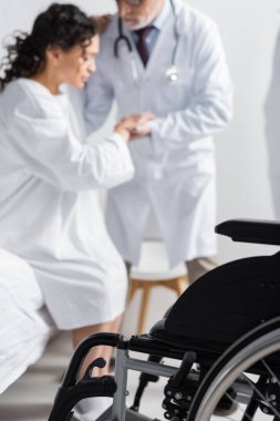 Doktorun yanındaki seçici tekerlekli sandalye odağı, Afrikalı Amerikalı bir kadının klinikte yataktan kalkmasına yardım ediyor.