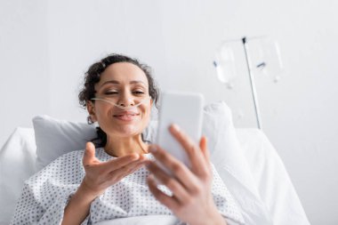 cheerful african american woman pointing at mobile phone on blurred foreground clipart