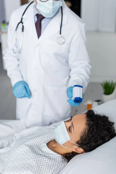 Läkare Mäta Temperaturen Afrikansk Amerikansk Kvinna Medicinsk Mask Med Pyrometer — Stockfoto