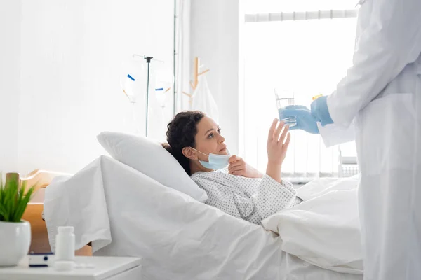 ラテックス手袋の医者はアフリカ系アメリカ人女性に病院のベッドで水を飲ませ — ストック写真