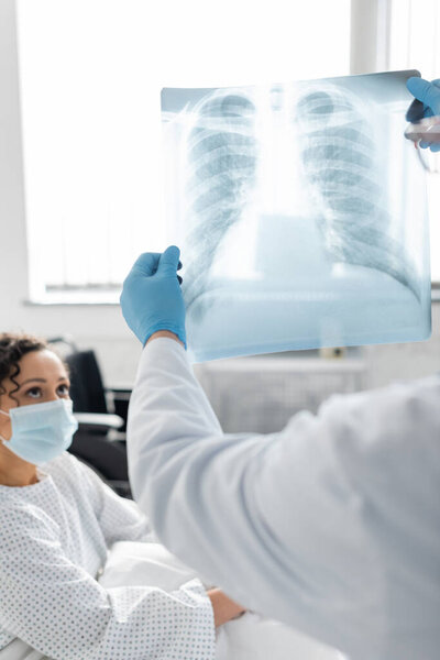 lungs x-ray in hands of doctor in latex gloves near african american woman in medical mask on blurred background