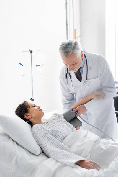 Врач надевает манжеты тонометра на руку больной африканской американки в клинике