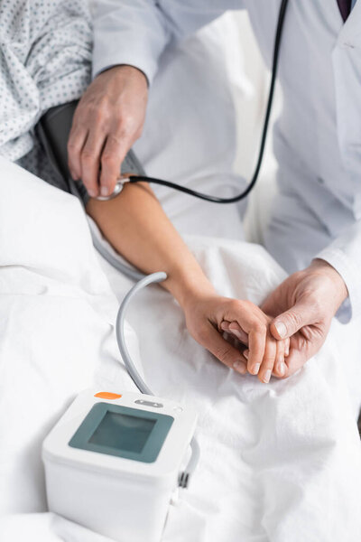 cropped view of doctor measuring blood pressure of woman in hospital