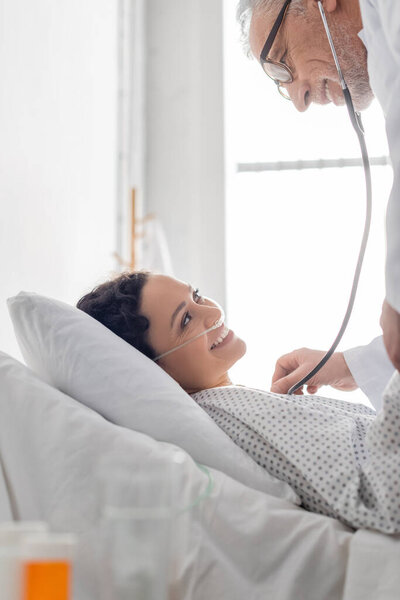 улыбающаяся африканская американка почти позитивный врач осматривает ее стетоскопом