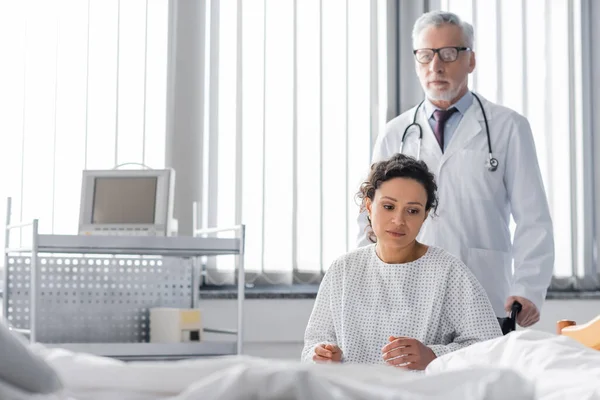 Traurige Afroamerikanerin Sitzt Rollstuhl Der Nähe Von Arzt Und Krankenhausbett — Stockfoto