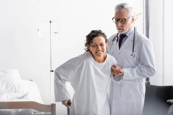 Mature Doctor Supporting African American Woman Frowning Pain While Walking — Stock Photo, Image