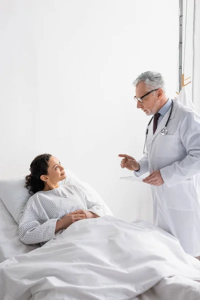 doctor with digital tablet talking to smiling african american woman in hospital