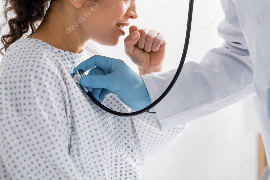 partial view of doctor in latex gloves examining coughing african american woman with stethoscope