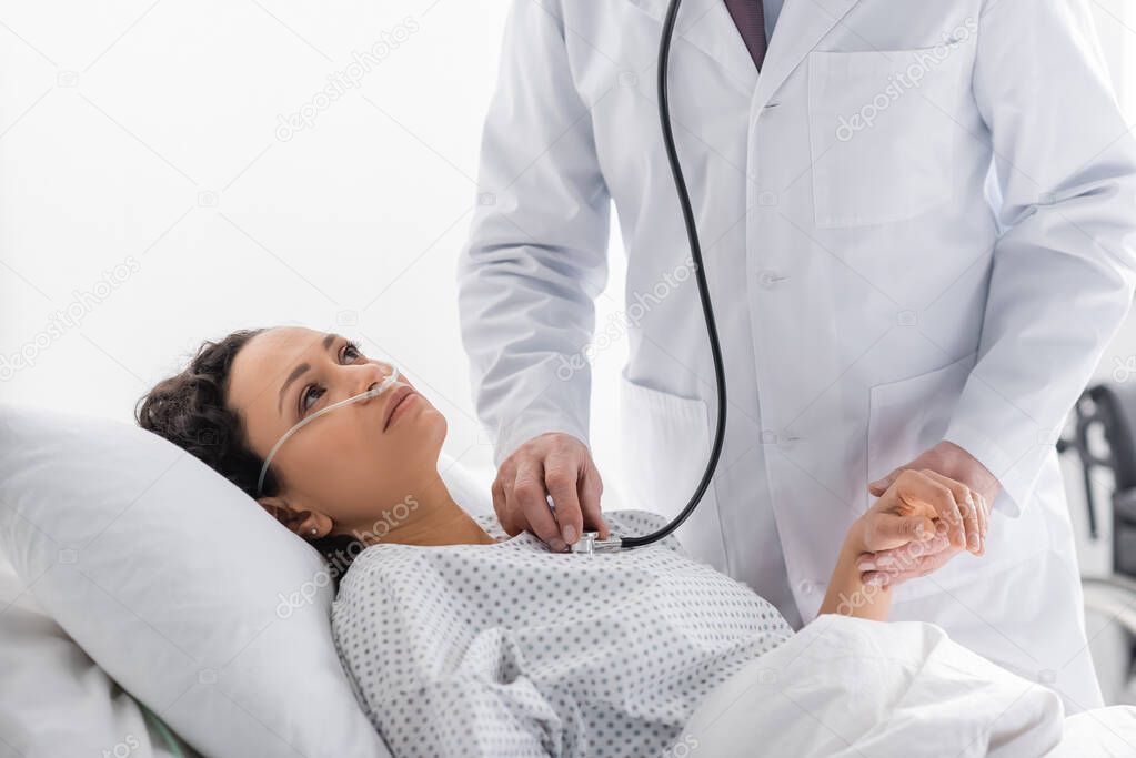 doctor holding hand of sick african american woman while examining her with stethoscope