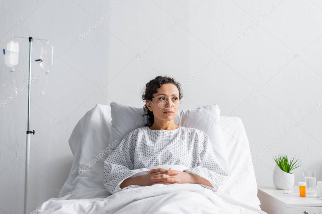 ill african american woman with nasal cannula sitting in hospital bed and looking away
