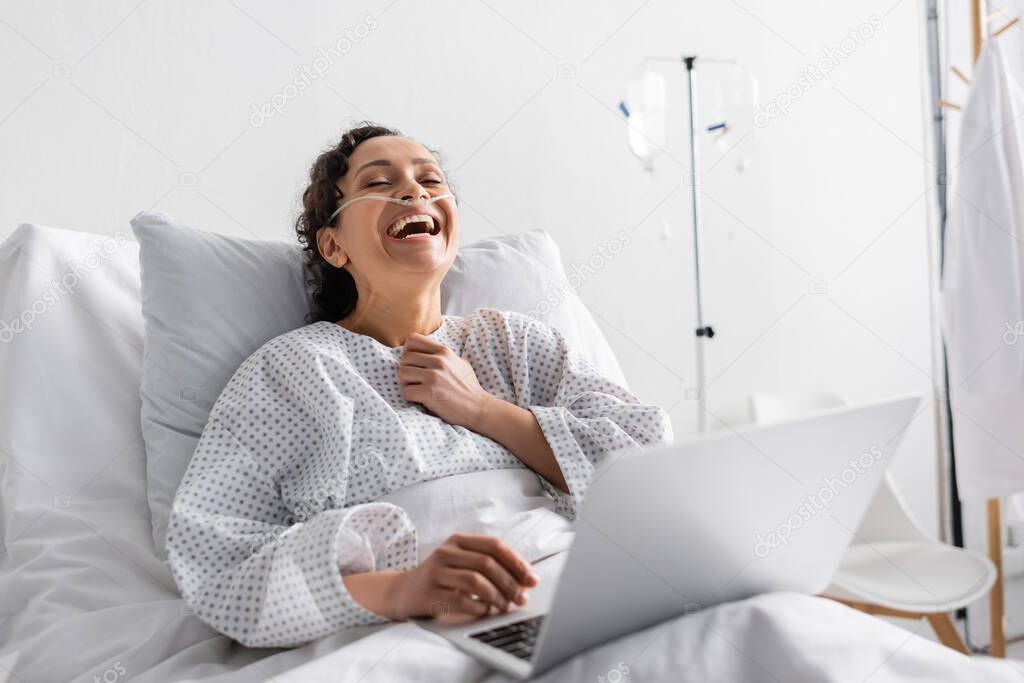 excited african american woman laughing while watching comedy film on laptop in hospital